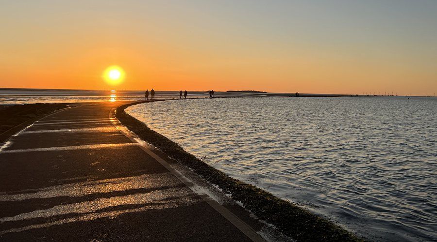Sunset over the Dee Estuary from the marine lake wall, with walkers silhouetted on the wall and Hilbre on the horizon