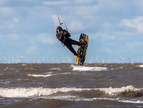 A kitesurfer mid-jump over choppy water with an offshore wind farm on the horizon